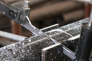 Industrial bandsaw with cooling liquid cutting a steel pipe. Shallow depth of field and motion blur.